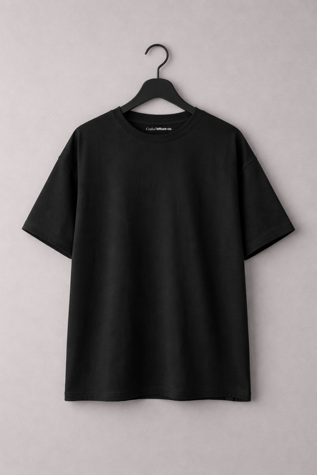 Black oversized cotton t-shirt hanging on a hanger with a relaxed fit and dropped shoulders